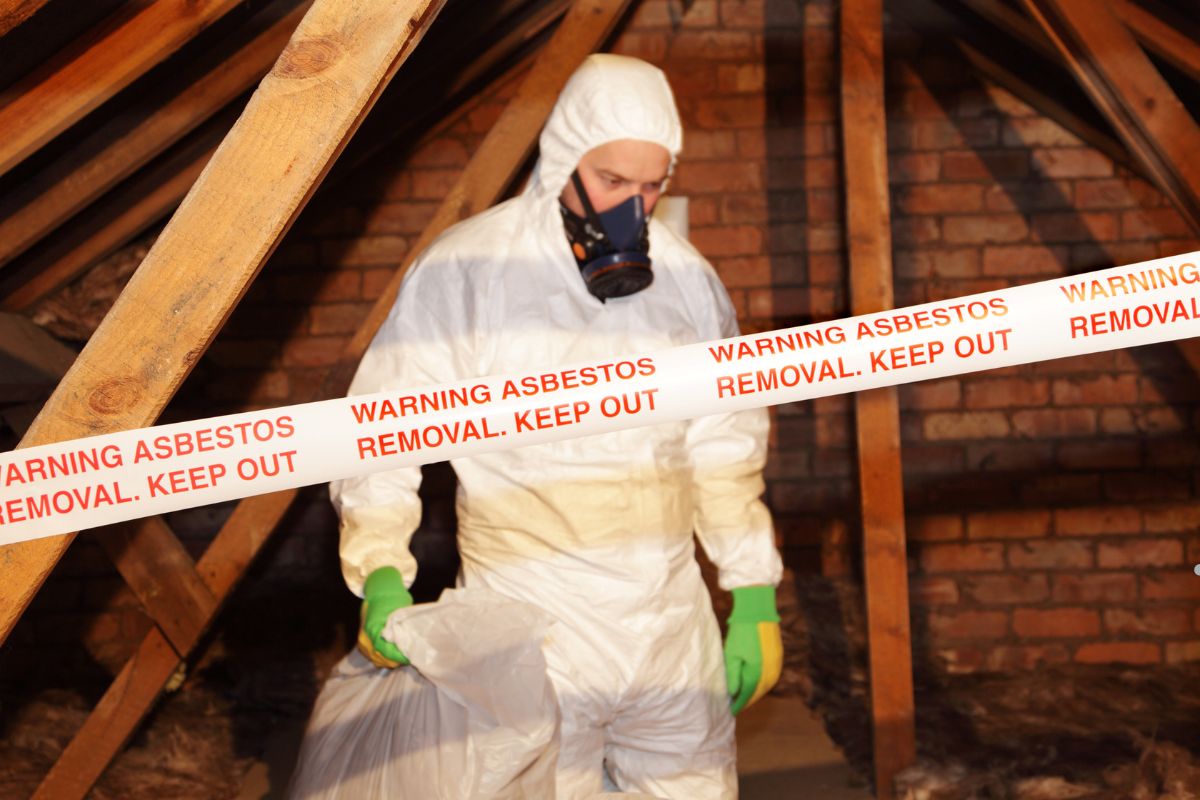 A man in a white protective suit and mask stands in an attic, conducting asbestos identification for mold removal services.