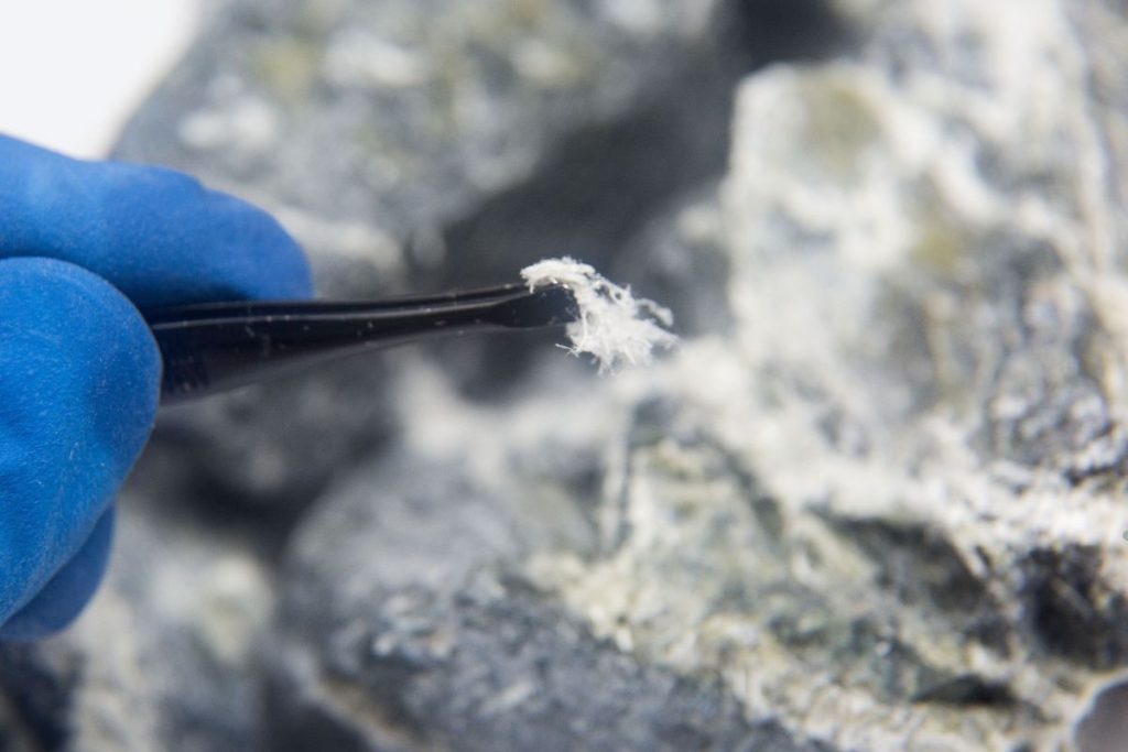 A person wearing blue gloves holds a toothbrush, indicating a focus on cleaning during an asbestos identification service.